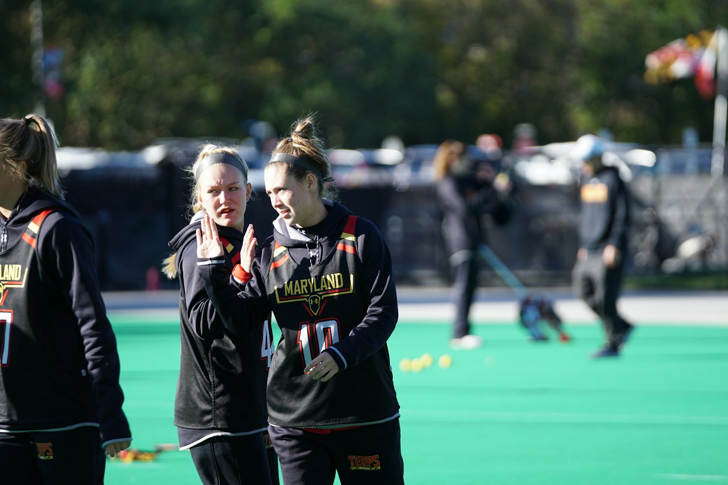 Two female athletes in team uniforms talking on a field.