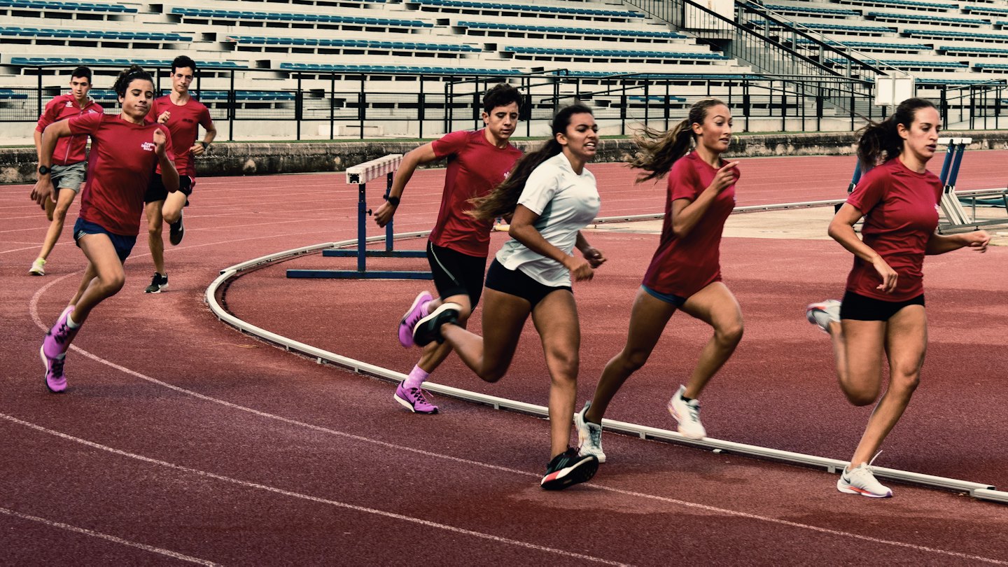 Seven athletes run together on a red track in a stadium.