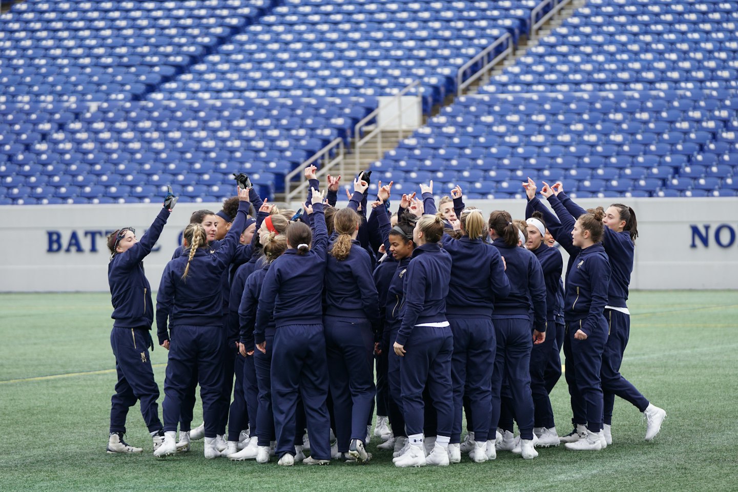 Athletes in navy tracksuits huddle together on a sports field.