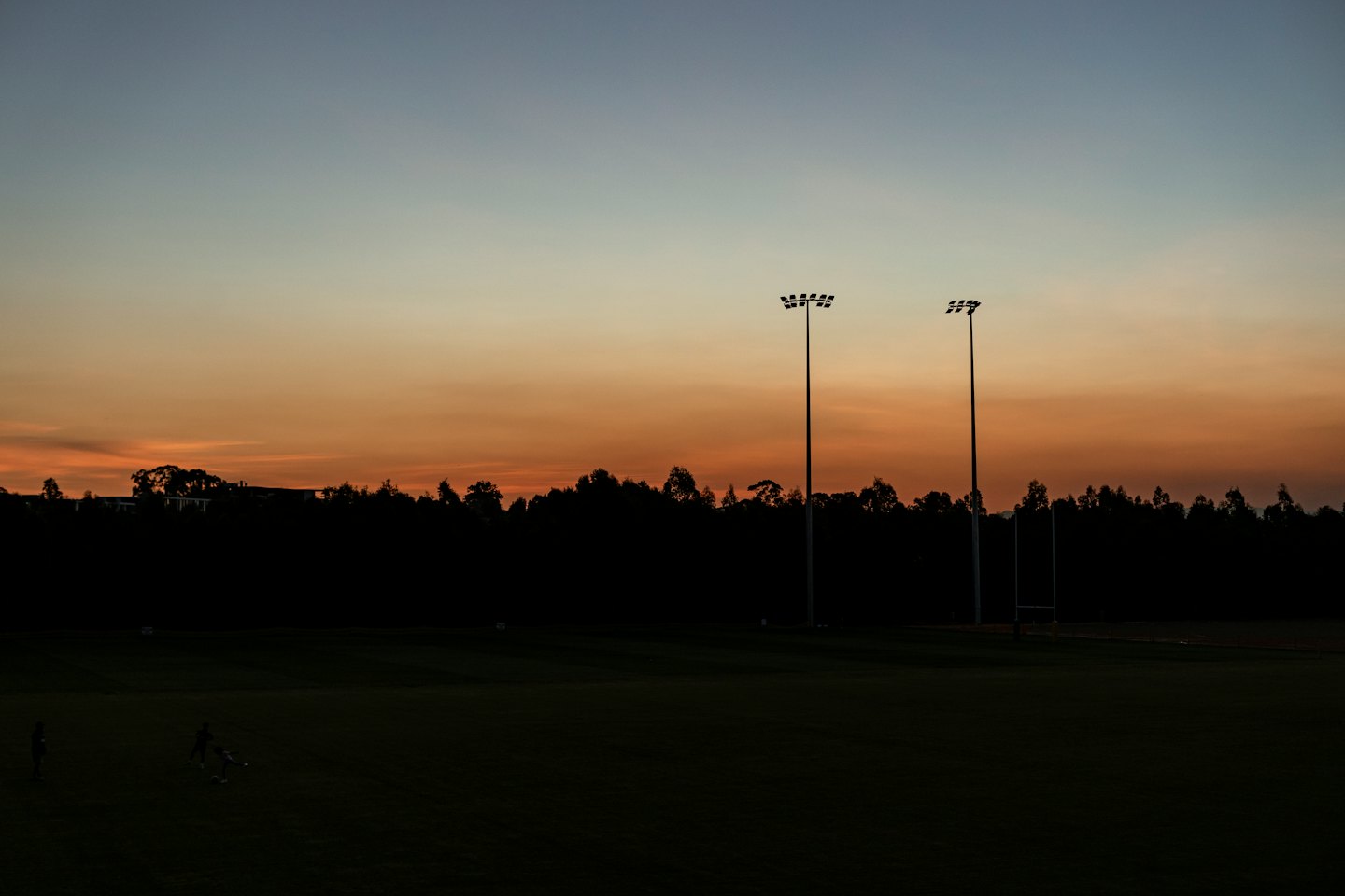 Sports field at dusk with two figures playing under stadium lights.