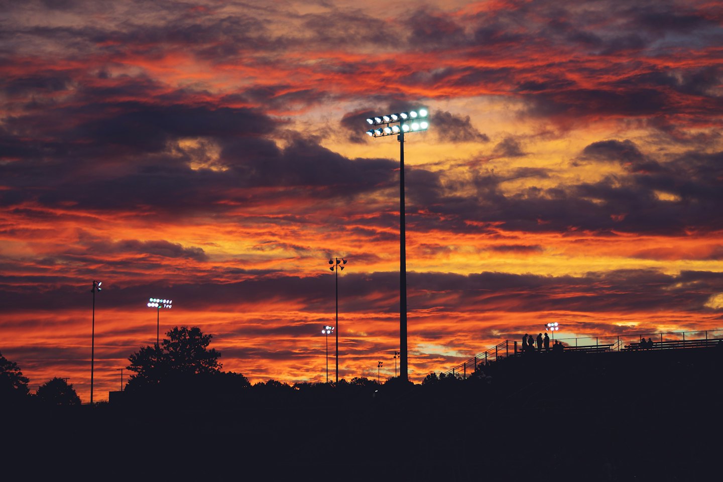 Floodlight poles tower over a sports field at sunset.