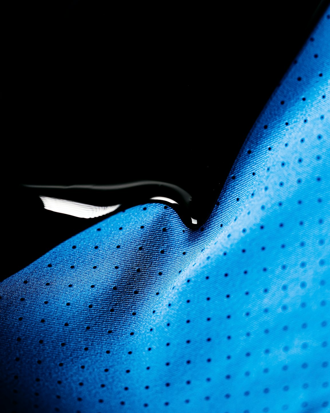 Blue perforated athletic fabric resting on a polished black surface.